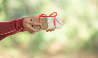 a woman holds a small gift box in beautiful hands. The girl is outdoors against the backdrop green leaves bokeh out of focus background from nature forest.